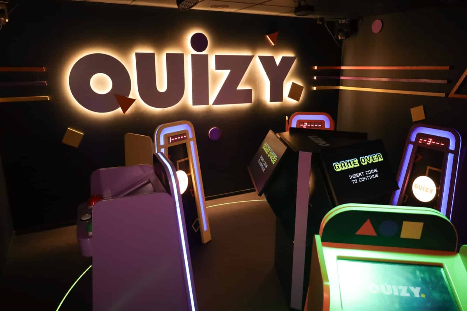 Quizy game show room with player stations and the lit Quizy sign